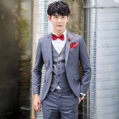 A man wears a slim-fit grey three-piece suit with a red bow tie and matching pocket square.
