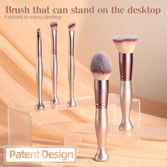 A set of rose gold makeup brushes with weighted bases designed to stand upright on a surface.