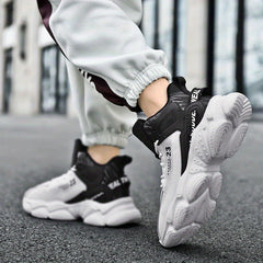 A pair of black and white mid-top lace-up sneakers with chunky rubber soles worn by a man.