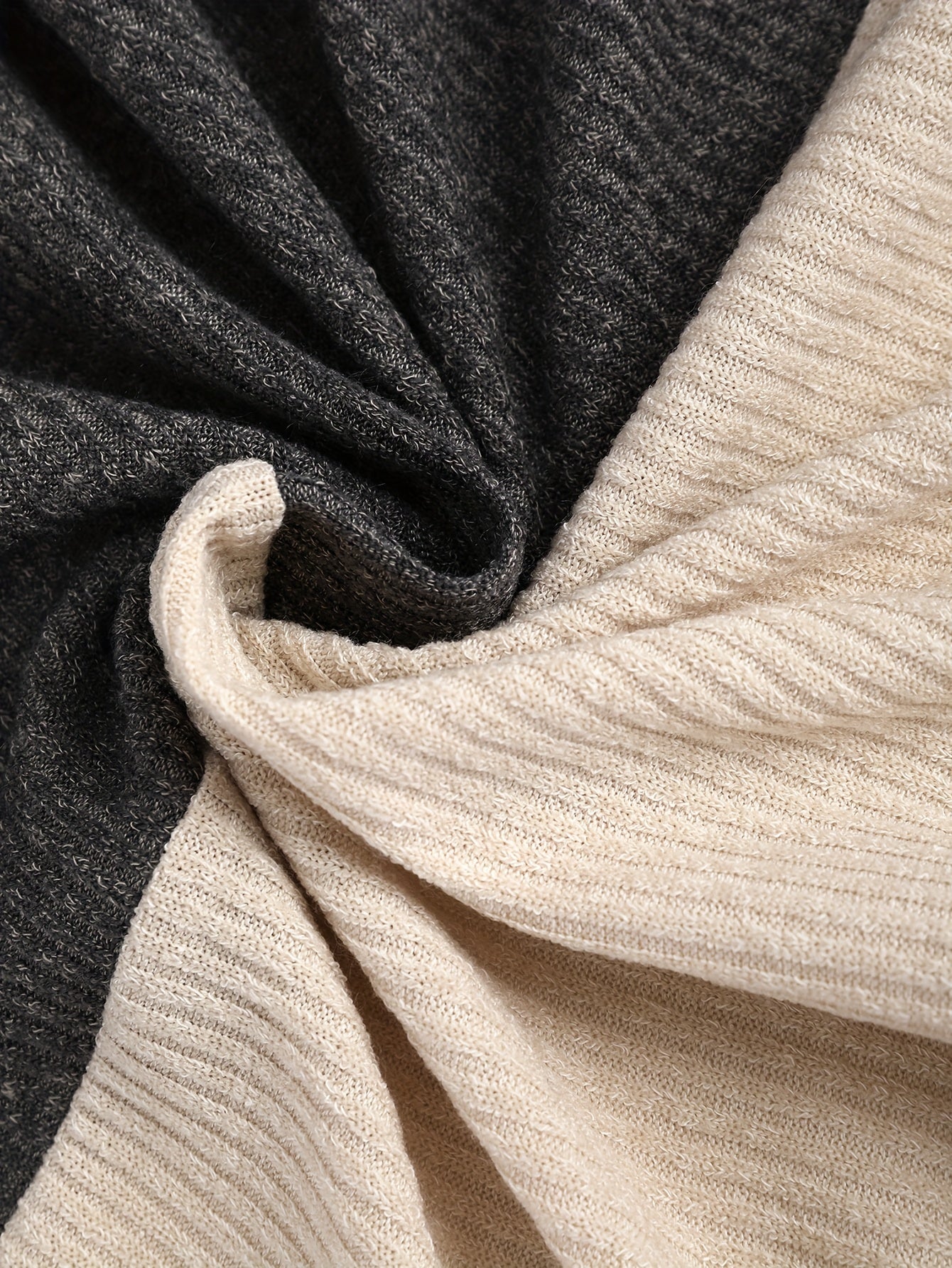 A close-up view of a soft, ribbed knit fabric featuring a color-block design in charcoal and beige.