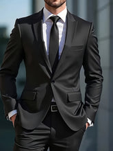 A man wears a classic black two-piece suit with a white shirt and black tie.