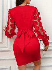 A woman wears a red bodycon dress featuring a large back bow and sheer sleeves with circular appliqués.