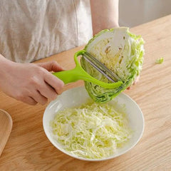 A person uses a green handheld cabbage slicer with stainless steel blades to shred cabbage.