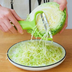 A person uses a green handheld cabbage slicer with a stainless steel blade to shred cabbage.