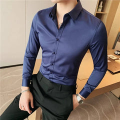 A man wears a slim-fit, long-sleeved navy blue button-up shirt with black trousers.
