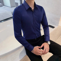 A man wears a slim-fit, long-sleeved navy blue button-up shirt with a turn-down collar.
