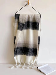 A long, fuzzy, black and white striped scarf with tasseled ends hanging from a hook.