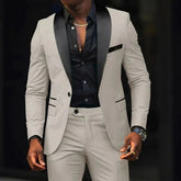 A man wears a slim-fit beige suit with a black shawl lapel and a matching black button-down shirt.