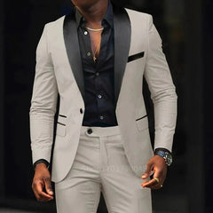A man wears a slim-fit beige suit with a black shawl lapel and a matching black button-down shirt.