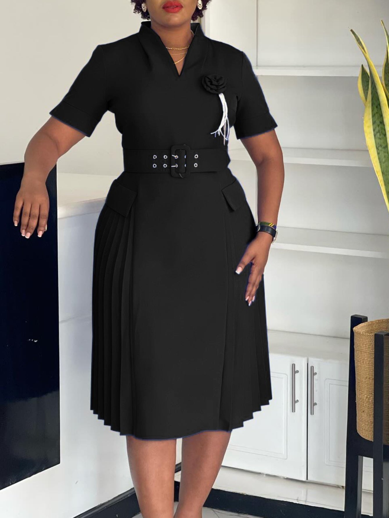 A black V-neck dress with a belted waist, short sleeves, and a pleated skirt.