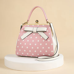 A pink and white polka dot handbag with a bow detail, kiss lock closure, and shoulder strap.