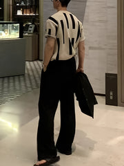 A man wears a short-sleeve, cream-colored knitted sweater featuring a black abstract block pattern.