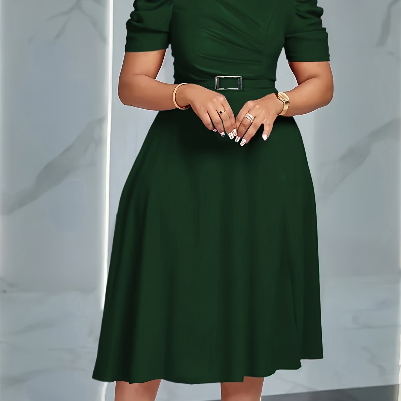 A woman wears a dark green, short-sleeved A-line dress with a belted waist.