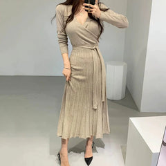 A beige long-sleeved V-neck knit dress with a wrap-style bodice and a pleated midi skirt.