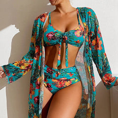 A woman wears a teal floral three-piece bikini set with a matching long-sleeved mesh cover-up.