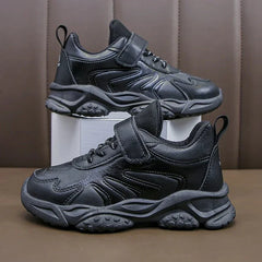 A pair of black children's sneakers with hook and loop closures and textured rubber outsoles.