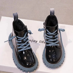 A pair of shiny black ankle boots for children with blue laces and thick lug soles.