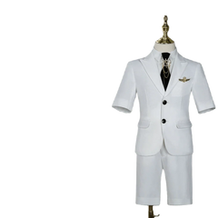 A white short-sleeved children's suit with a black tie and gold brooch on a mannequin.