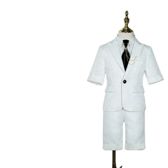 A white short-sleeved boys suit with a textured pattern, black tie, and gold chain accessory.