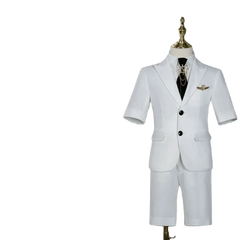 A white short-sleeved children's suit with a black tie and gold brooch on a mannequin.