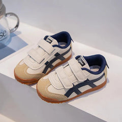 A pair of beige and navy blue children's sneakers with hook-and-loop straps and gum soles.