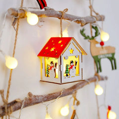 A wooden Christmas house ornament hangs from a rustic branch decorated with string lights.