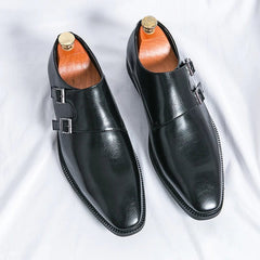 A pair of black leather double monk strap dress shoes with a pointed toe and silver buckles.