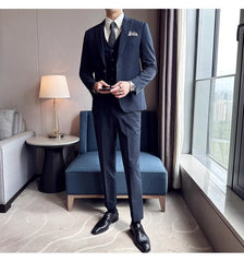 A man wears a slim-fit navy blue three-piece suit with a white shirt and black dress shoes.