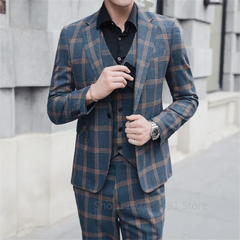 A man wears a blue plaid three-piece suit with a black shirt and a silver watch.