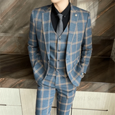 A man wears a blue plaid three-piece suit with a black shirt and grey tie.