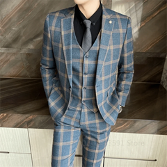 A man wears a blue plaid three-piece suit with a black shirt and grey tie.