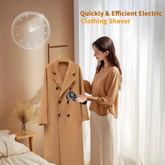 A woman uses a black handheld electric fabric shaver on a tan wool coat hanging in a room.