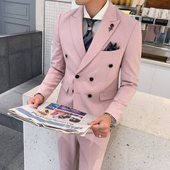 A man wears a slim-fit light pink double-breasted suit with a patterned tie and rose lapel pin.