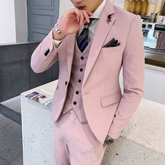 A man wears a slim-fit, light pink three-piece suit with a patterned tie and a lapel pin.