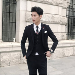 A man wears a slim-fit black three-piece suit with a white shirt and a striped tie.