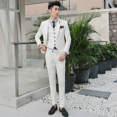 A man wears a slim-fit white three-piece suit with a striped shirt and dark loafers.