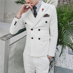 A man wears a white slim-fit double-breasted suit with a striped shirt and rose lapel pin.