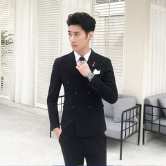 A man wears a slim-fit black double-breasted suit with a white shirt and a red rose lapel pin.