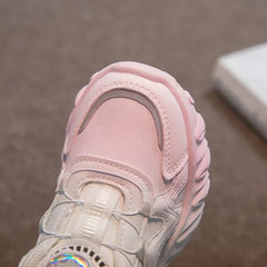 A close-up of a light pink children's sneaker featuring a mesh upper and a chunky rubber sole.