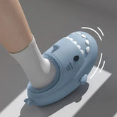 A person wears a blue shark-shaped plush slipper with a cartoon face and white teeth.