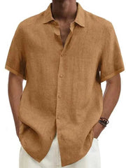 A man wears a solid tan short-sleeved button-down shirt made of a linen-blend fabric.