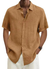 A man wears a short-sleeved, tan-colored linen button-down shirt with a collar.