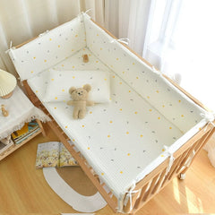 A white quilted crib bumper with a yellow moon and star pattern inside a wooden baby crib.