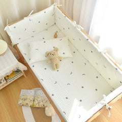 A white crib bumper set with a grey moon and star pattern inside a wooden baby crib.