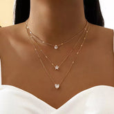 A gold-toned layered necklace set featuring a teardrop, star, and heart crystal pendant.