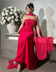 A sleeveless red satin floor-length evening gown featuring a beaded bodice and a matching sash.