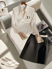 A cream-colored long-sleeve formal shirt with a gold D logo and metallic cuffs.