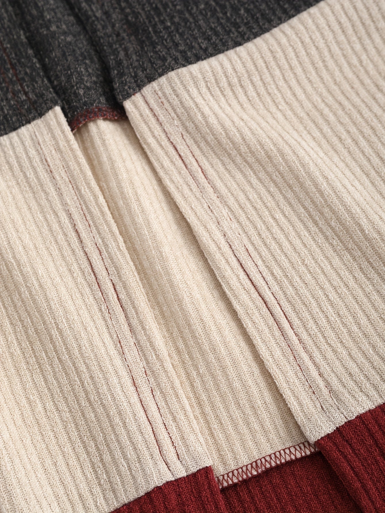 A close-up view of a color-blocked ribbed knit cardigan featuring dark gray, cream, and maroon.