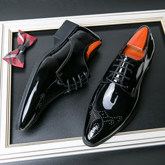 A pair of black patent leather pointed-toe dress shoes with lace-up closures and decorative studs.