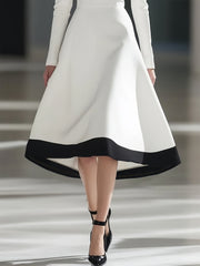 A woman wears a white midi dress with a black hem and long sleeves in an A-line silhouette.